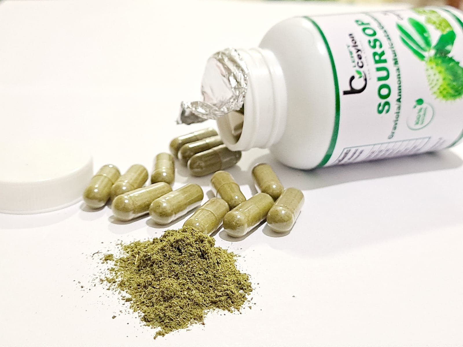 Leafy Ceylon soursop bottle lying beside capsules and leaf powder