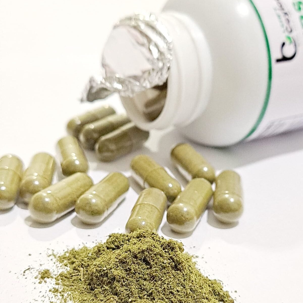 Open soursop capsule bottle beside capsules and green leaf powder