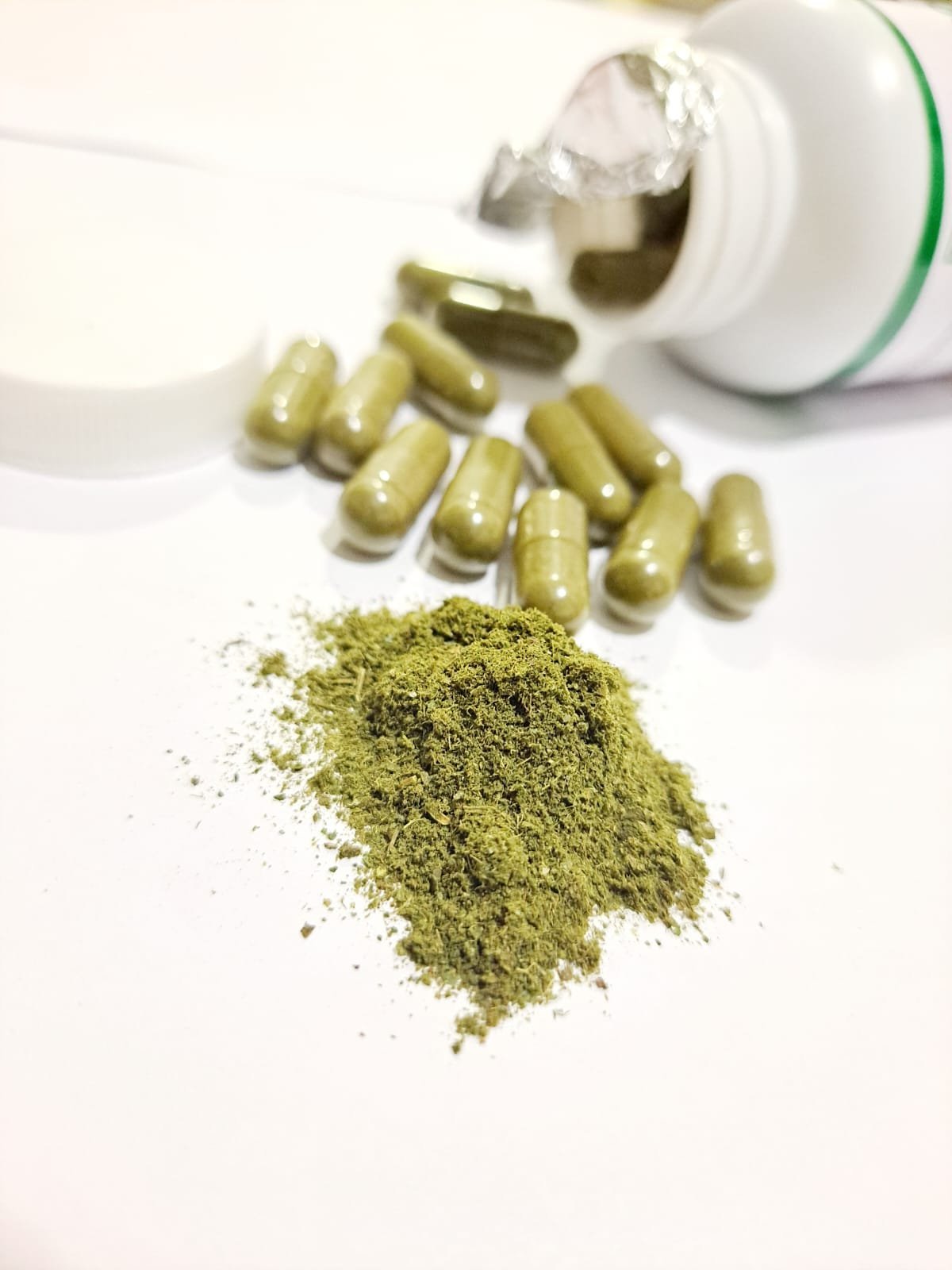 Capsules and green powder spilling from a white bottle